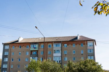 Parlak mavi gökyüzünün altında ağaçların arasında huzur içinde duran bir apartman dairesi huzurlu bir yerleşim bölgesinde renkli süslemelerle balkonlar sergiliyor..