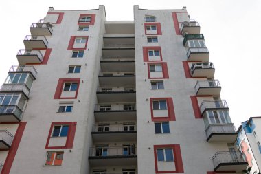 Renkli aksanlar ve sayısız balkonların yer aldığı yüksek bir konut binası göze çarpıyor. Yapı, canlı bir mahallede yaşayan çağdaş kentsel yaşamı yansıtıyor..