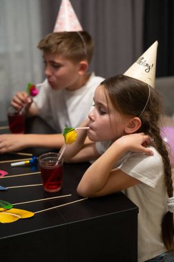 Çocuklar bir doğum günü kutlamasıyla çok meşguller, renkli içecekler yudumluyorlar ve lezzetli tatlıların tadını çıkarıyorlar, neşeli parti şapkaları giyiyorlar, neşeli dekorasyonlarla çevrili..