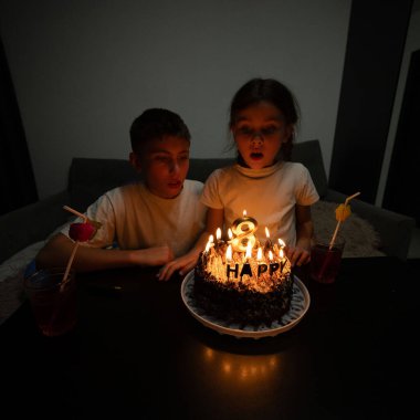 Sevinçten havalara uçmuş iki çocuk, güzel dekore edilmiş bir doğum günü pastasının etrafında mum yakarak, samimi bir akşam ortamında özel bir olayı kutluyorlar..