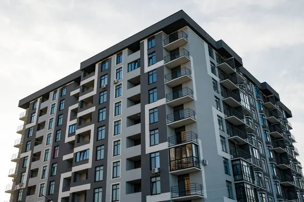 Şık, modern bir apartman, şehir ortamında çok sayıda pencere ve balkonun yer aldığı, bulutlu bir gökyüzünün altında çağdaş tasarımın özünü yansıtan yüksek bir bina..