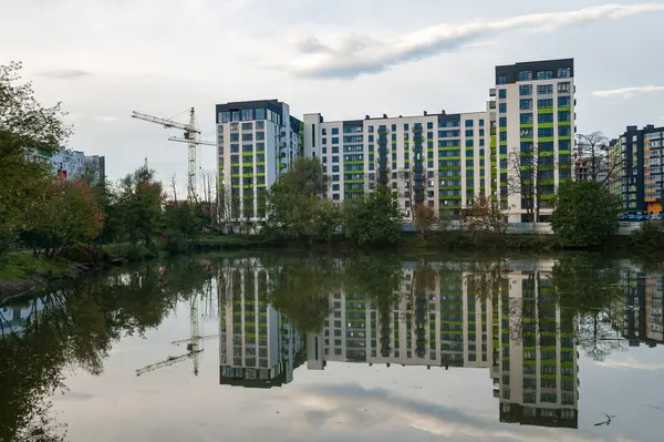 Çağdaş binaların yansımalarını yansıtan sakin bir şehir göleti, yakınlardaki ağaçlar bulutlu bir öğleden sonra rüzgarda hafifçe sallanırken,.