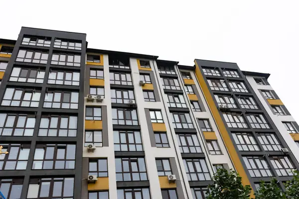 Parlak, modern konut yapısı bulutlu bir gökyüzüne karşı dimdik ayakta duruyor, büyük pencereli cesur mimari, doğal ışığı konutlara davet ediyor..