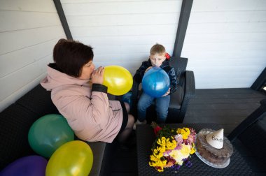 Bir kadın ve bir çocuk keyifli bir öğleden sonra paylaşıyorlar. Çiçekler ve pastayla süslenmiş büyüleyici bir alanda otururken renkli balonlar..