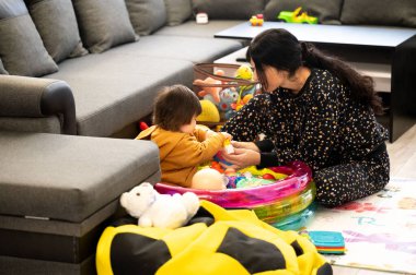 Bir anne, renkli oyuncaklarla ve sıcak bir atmosferle çevrili rahat bir oturma odasında, neşeli aktivitelere girişir..