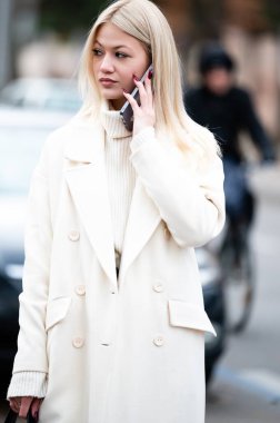 Kalabalık bir şehir zemininin ortasında, beyaz önlüklü şık bir şahıs telefonda konuşuyor, yoğun şehir akışına karşı modern karmaşıklığı somutlaştırıyor..