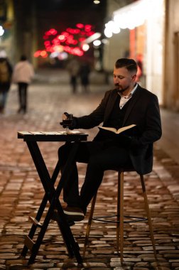 İyi giyimli bir adamın, parlak şehir ışıklarının arasında kendini kitaplarına kaptırıp, canlı bir atmosferde sükunetin özünü yakaladığı sessiz anlar..
