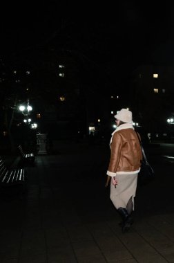 Şık bir birey, rahat bir giysi ve şapkayla, huzurlu bir yalnızlık ortamı yaratarak, gece huzur dolu bir parkta yürüyor.