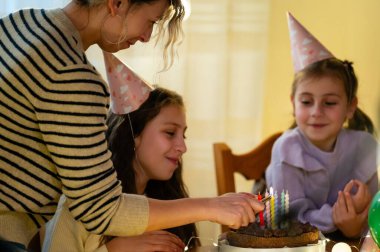 Neşeli arkadaşlar bir çikolatalı pastanın etrafında toplanıp kutlama yaparken doğum günü mumlarını yakıyorlar. Odanın sıcacık parıltısı neşeli atmosferi güçlendirir ve kahkahalar havayı doldurur..