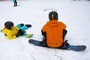 İki arkadaş kar kaplı yamaçlarda, parlak kış giysileri içinde, dağ zemininde snowboard yapmanın keyfini çıkarıyorlar..