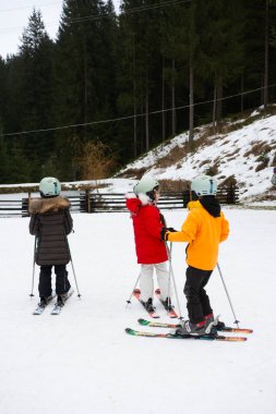 Renkli kayak kıyafetleri içinde bir grup çocuk kar yamacında toplandı. Kayak derslerine hazırlanırken heyecanlı görünüyorlar..