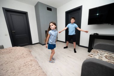 İki çocuk parlak, çağdaş bir oturma odasında şakalaşarak dans ediyorlar. Atmosfer, birlikte hareketli bir iç aktiviteye girerken neşeyle doludur..