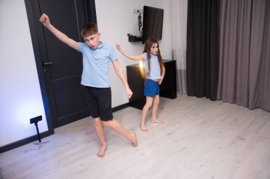 İki çocuk, doğal ışık ve neşeli ruhla dolu rahat bir oturma odasında dans ederken coşkuyla ışıldıyor ve keyifli bir atmosfer yaratıyorlar..