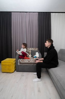 İki çocuk rahat bir oturma odasında oturmuş, renkli mobilyalarla çevrili bir öğleden sonra video oyunları oynuyor ve neşe ve kahkaha anlarını paylaşıyorlar..