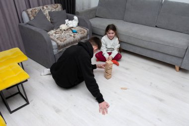 Sıcak bir yaşam alanında, bir çocuk ve bir yetişkin eğlenceli bir aktiviteye girişir, ahşap blokları yığar ve akşam ışığında birlikte inşa ederlerken kahkahalarını paylaşırlar..