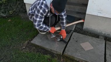 Kendini işine adamış bir işçi, öğleden sonra geç saatlerde şık bir konut bahçesinde pürüzsüz bir yol için çimenlerin üzerinde diz çöker taş levhalar öğütür..