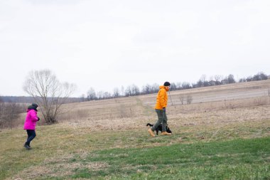 İki birey serin bir günde sakin kırsal alanlarda dolaşırken bir köpek onlarla birlikte mutlu bir şekilde koşuyor, baharın erken zamanlarındaki güzelliği alıyor..