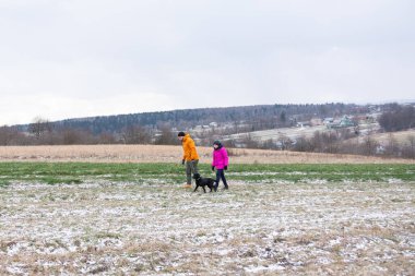 İki figür, sadık bir köpekle karlı bir arazide yan yana yürüyor..