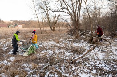 Children and adults work together to collect firewood in a snowy field, enjoying the crisp winter air while fostering connections with nature and each other.