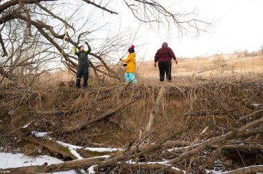 Üç arkadaş, yaprakları dökülmüş, renkli kış kıyafetleriyle sarmalanmış, doğanın güzelliğini kucaklarken kahkahalarını ve yoldaşlıklarını paylaşarak nehir kıyısında yürür..