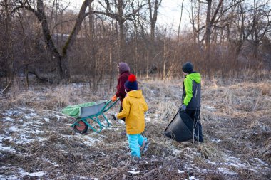 Renkli ceketler giymiş üç çocuk kış manzarasında dalları ve yaprakları toplayıp doğanın ortasındaki oyunculuk ve takım çalışmasını somutlaştırmaya giriştiler..