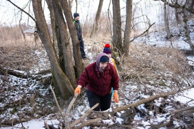 İnsanlar, karlı bir bölgede ağaçların arasından düşen dalları toplayarak ısınmak için malzeme bulduklarında kışın serin havasını deneyimlemekle meşguller..