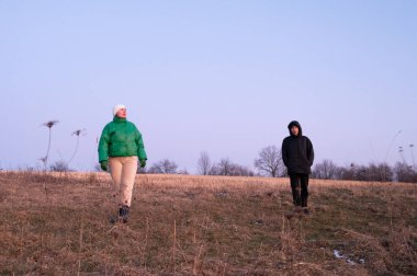 İki arkadaş, serin akşam havası için sıcacık giyinmiş, alacakaranlıkta sakin açık bir alanda geziniyor, doğanın barışçıl atmosferinin tadını çıkarıyor..