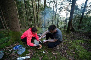 İki arkadaş, sakin bir ormanda açık bir ateşin üzerinde yemek pişirmeyi, malzemeleri toplamayı ve doğanın güzelliği ve temiz havasının tadını çıkarmayı severler..