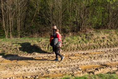 Ilık bir bahar öğleden sonrasında doğanın güzelliğinin tadını çıkaran, parlak bir güneşin altında canlı yeşilliklerle çevrili çamurlu bir patikada yürüyen iki kişi..