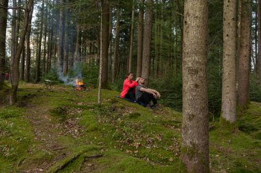 Etrafı uzun ağaçlarla çevrili, birkaç tanesi sıcak bir kamp ateşiyle rahatlıyor, güneş öğleden sonra yaprakların arasından süzülürken doğanın sessizliğinin tadını çıkarıyorlar..