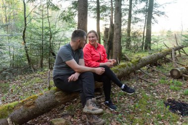 Sohbete dalmış bir çift, birlikte düşmüş bir kütüğün üzerinde oturur ve akşam yaklaşırken ormanın canlı yeşilliği arasında huzurlu bir anı paylaşır..