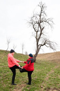 İki arkadaş neşeli bir aktiviteye girişiyor, tebessümlerini paylaşırken bacaklarını çimenli bir tarlada kaldırıyorlar, başlarının üzerinde bulutlu bir gökyüzü ile ilkbaharın dinginliği ile çevrelenmiş..