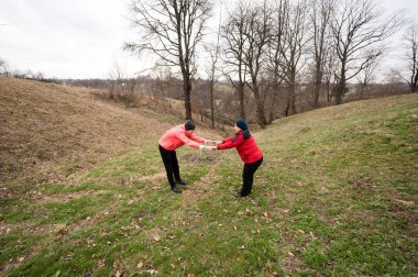 Parlak kırmızı ceketli iki insan, çimenli bir yamaçta, açık kalpli bir ruhla birbirlerini çekiyorlar. Etrafı çıplak ağaçlarla çevrili ve baharın ilk zamanlarından kalma ipuçlarıyla çevrili..