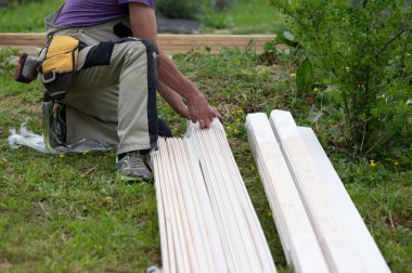 İşçi bir çardak inşa etmek için beyaz tahtaları açıyor, kurulum işi.