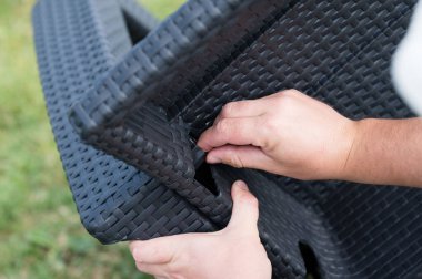 Koyu renkli örülmüş plastik mobilyaları birleştiren ellerin yakın çekimi. Kişi yapının iki parçasını birbirine bağlıyor..