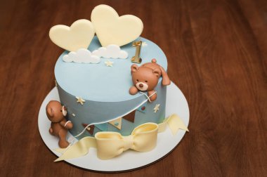 Sevimli oyuncak ayılar, kalpler ve bir numarayla süslenmiş enfes bir ilk doğum günü pastası. Pastel mavisi krema ve sarı aksanlar büyüleyici ve tatlı bir tasarım yaratır..