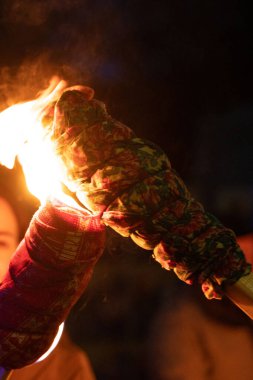 Geceleri birinin tuttuğu yanan bir meşalenin yakın çekimi. Bir insanın yüzü arka planda hafifçe bulanıklaşır. Parlak bir ay karanlık gökyüzünde kısmen görünür..