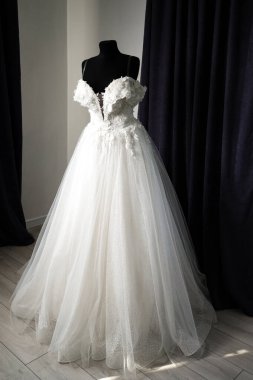 Omzundan kopan kayışlar ve çiçekli detayların yer aldığı çarpıcı bir gelinlik, bir mankenin üzerinde sergileniyor. Elbise narin tül kumaştan ince titreşimler alıyor..