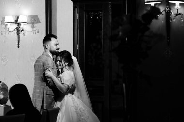 Düğün törenlerinde bir gelin ve damadın hassas bir anını paylaştığı siyah beyaz bir fotoğraf. Çift şık bir şekilde giyinmiş ve ortam rafine edilmiş..