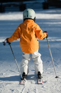 Genç kayakçı, güneşli bir yamacın tepesinde kendine güvenle duruyor. Dağlarda serin bir kış günü taze karları oymanın heyecanını tatmaya hazır..