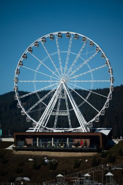 Parlak güneş ışığı, gondolları ziyaretçiler için hazırlanmış büyük gözlem çarkını aydınlatıyor..