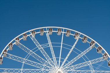 Çarpıcı dev bir tekerlek dimdik duruyor, kamaraları ziyaretçileri yeni yüksekliklere taşımaya hazır, parlak, neşeli bir günde dramatik bir zemin oluşturan canlı mavi gökyüzü.