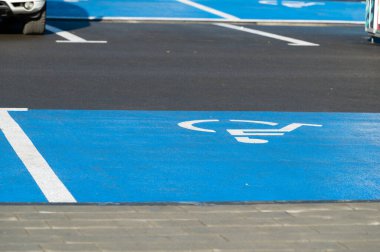 Erişilebilirlik için ayrılmış açık mavi park yerleri hareketli bir alışveriş alanında, sıcak öğleden sonra güneşinin altında arabaların park yeri olarak kapsayıcılığı teşvik ediyor..