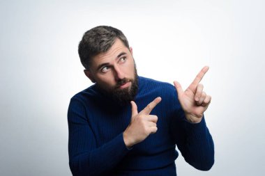 Mavi süveterli sakallı bir adam işaret parmağıyla yukarı ve yana bakıyor, hareketini takip ediyor. Meraklı görünüyor ya da dikkat çekiyor..