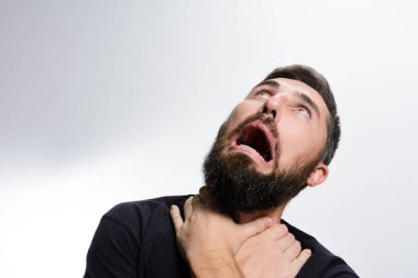 Sakallı bir adam boğazını tutar, yüzü çığlıkla buruşur, şiddetli bir korku, panik ve kaygı taşır..