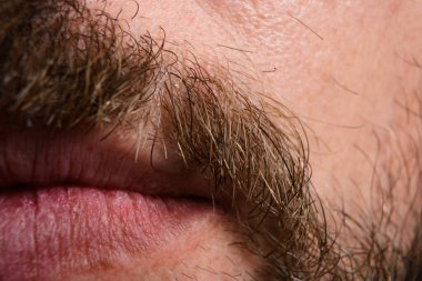 Bir adamın ağzının detaylı makro görüntüsü, dudaklarının dokusunu ve bıyığının tek tek kıllarını gösteriyor. Görüntü, yüz hatlarının ince detaylarını vurgular.