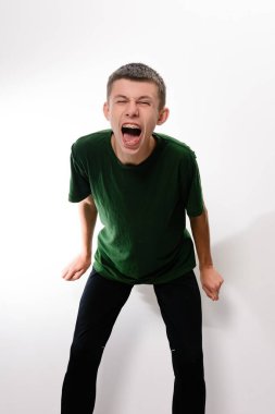 Kısa kahverengi saçlı, koyu yeşil gömlekli ve siyah pantolonlu genç bir adam ağzı açık bağırıyor. Resim düz beyaz bir arkaplan üzerinde ayarlanır.