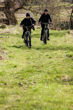 Dağ bisikleti süren iki genç insan bir tarlada bir yol boyunca bisiklet sürüyor. Güneş ışığı sahneyi aydınlatır, parlak ve neşeli bir atmosfer yaratır..