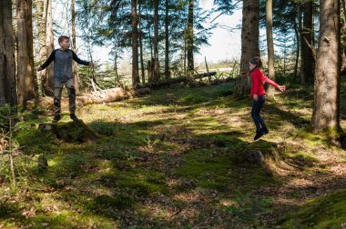 İki genç çocuk güneşli bir günün tadını çıkarıyorlar, gür, yosunlu orman zemininde ağaçların üzerinde neşeli bir şekilde zıplıyorlar. Güneş ışığı ağaçların arasından süzülüp büyülü bir atmosfer yaratır..