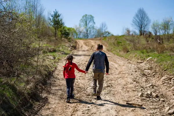 İki küçük kardeş, bir erkek ve bir kız, kırsal bir patikada el ele yürüyorlar. Güneşli bir gün ve doğal manzara huzur verici ve iç açıcı bir manzara yaratır..